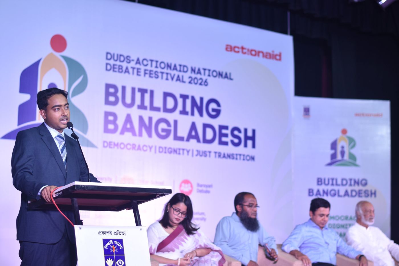 Shazid speaking at the podium in front of the Building Bangladesh festival banner