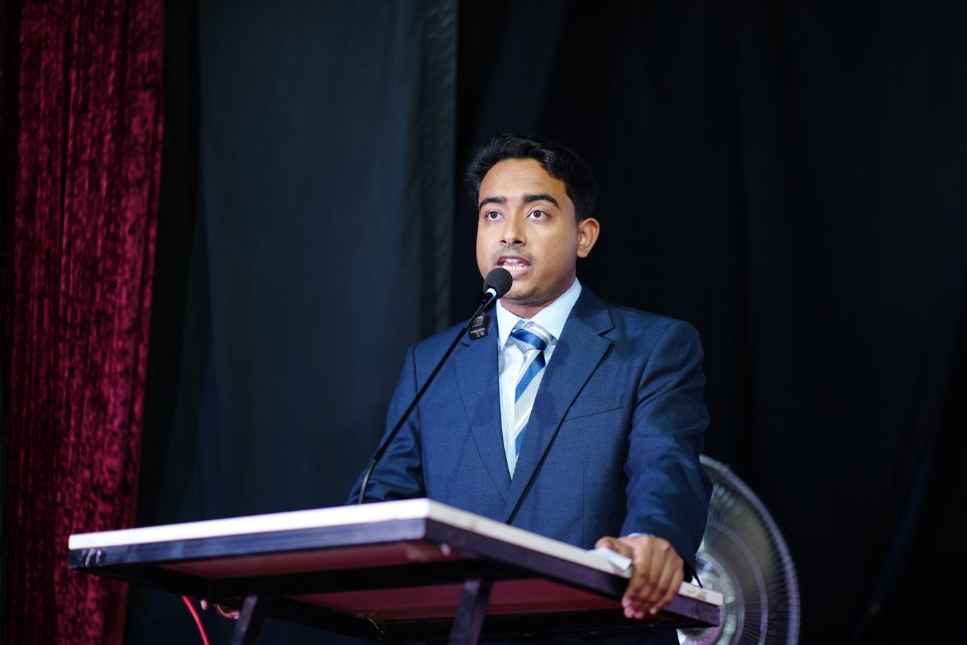 Shazid speaking at a podium on a dark stage